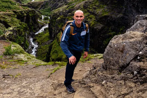 Paweł Lenar z plecakiem wchodzi pod górę nad doliną z rzeką i uśmiecha się