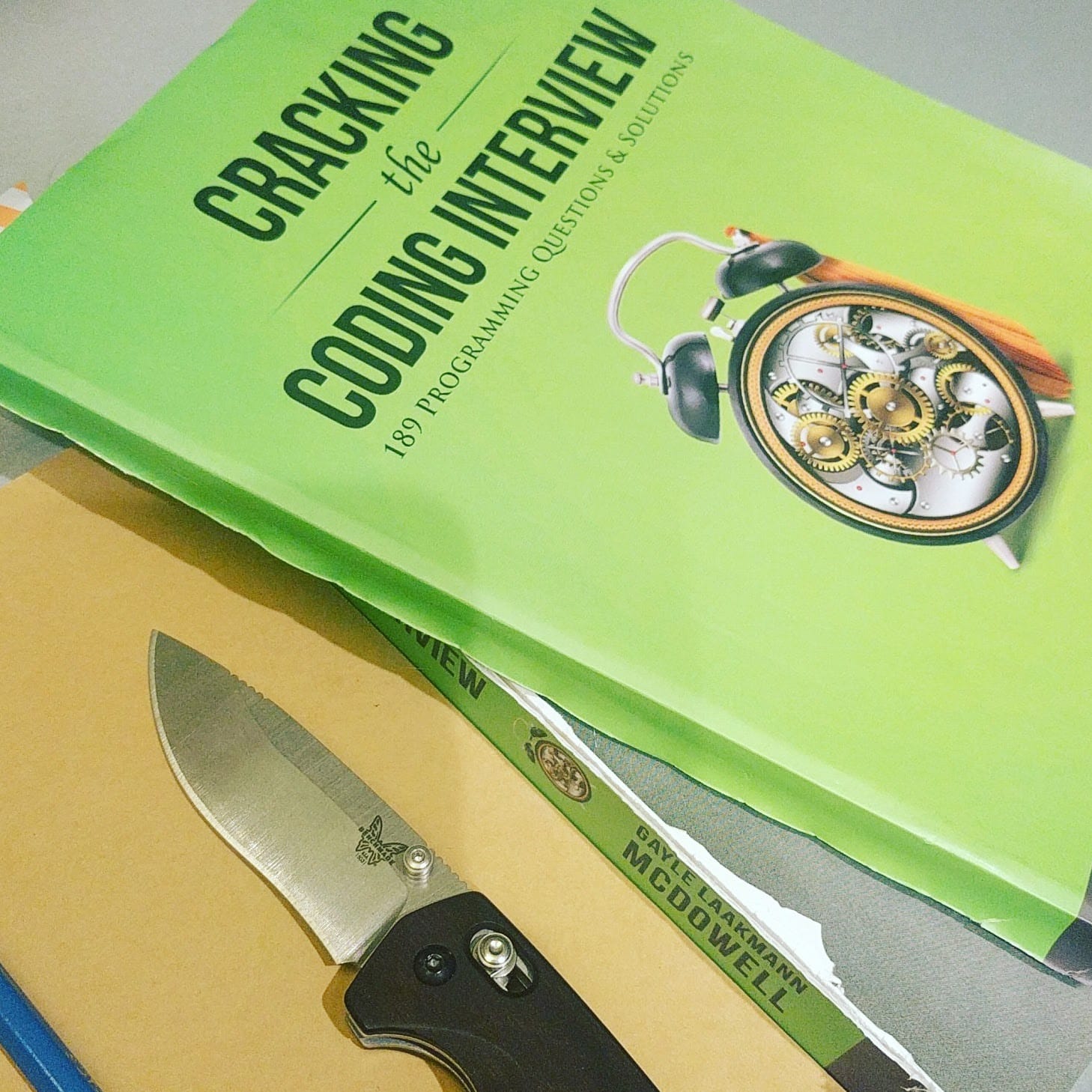 Photo of a pocket knife next to a copy of "Cracking the Coding Interview." The spine has been cut to lighten the book