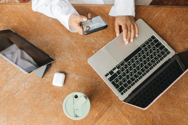 Person using mobile phone and laptop on desk working.
