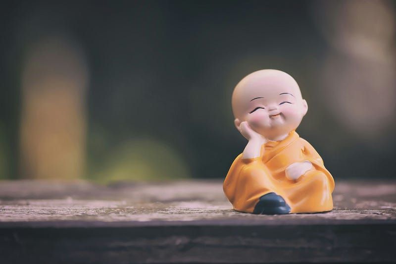 a tiny Buddha sculpture with one hand on his cheek and a smile