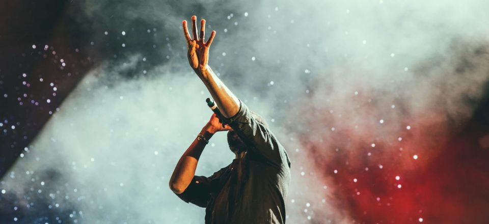 Singer performing live on stage with raised hand, concert lights and smoke in the background