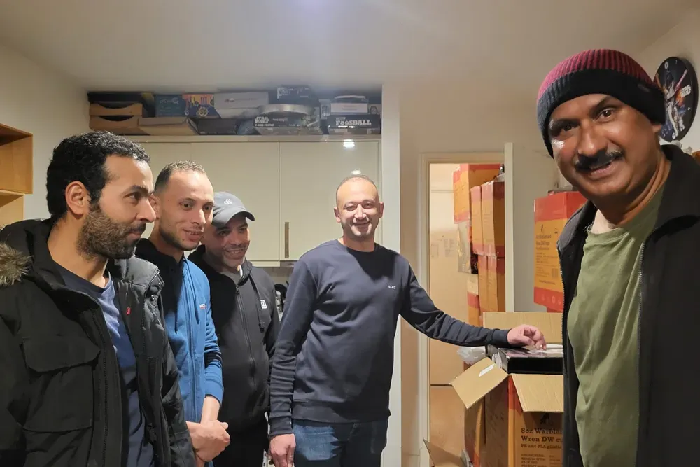 Five men standing in a small apartment.