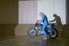 Stephen Skrynka on a motorcycle next to his wooden Wall of Death, casting a shadow on it.