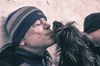 A man standing against a wall gets a kiss from a shaggy dog.