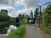 A cyclist in a yellow jacket emerges from under a bridge, in the right of the image. In the left, is a canal. The sky is dram