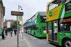 Two green buses are on the right side of the picture, one drawing into a bus stop and the other drawing away. On the left of