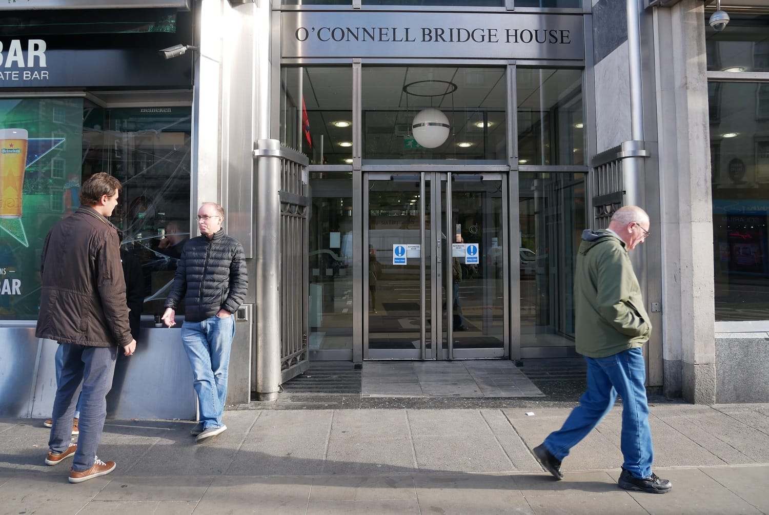 The big glass doors at the entrance to the offices of the Residential Tenancies Board. One man walks by, and two stand talking in the left of the photo.