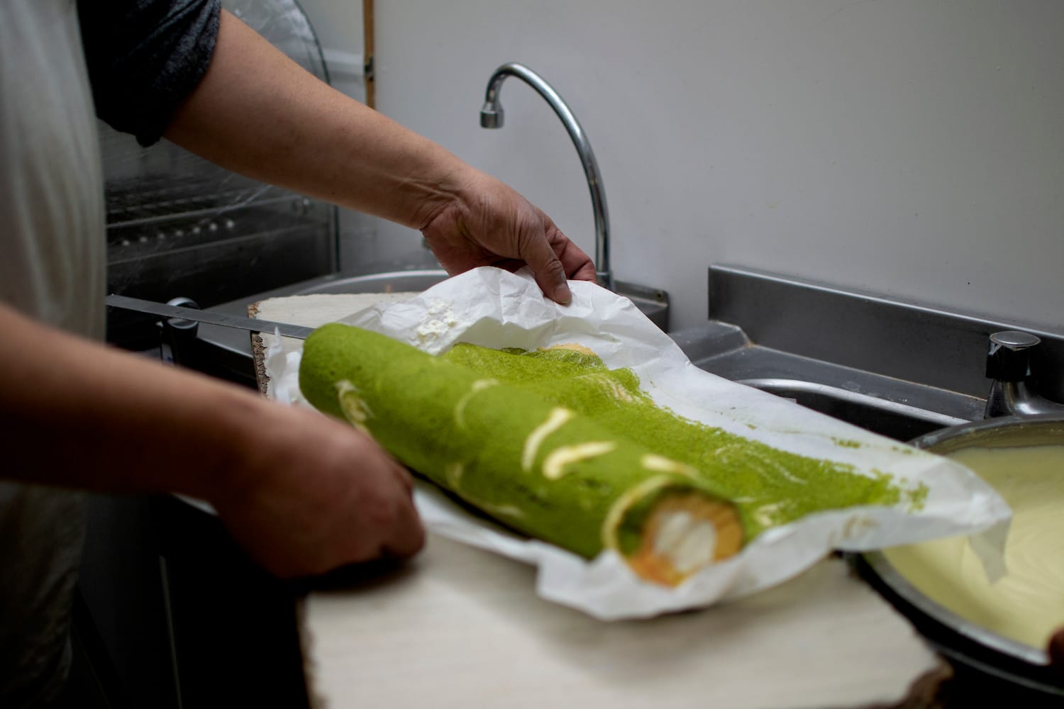 Somebody rolls a log of matcha roll on some baking paper.