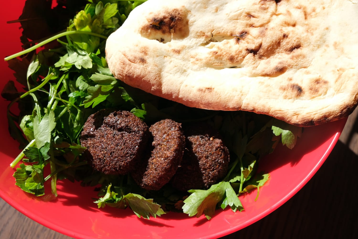 A flat bread and three round falafal and some salad leaves.