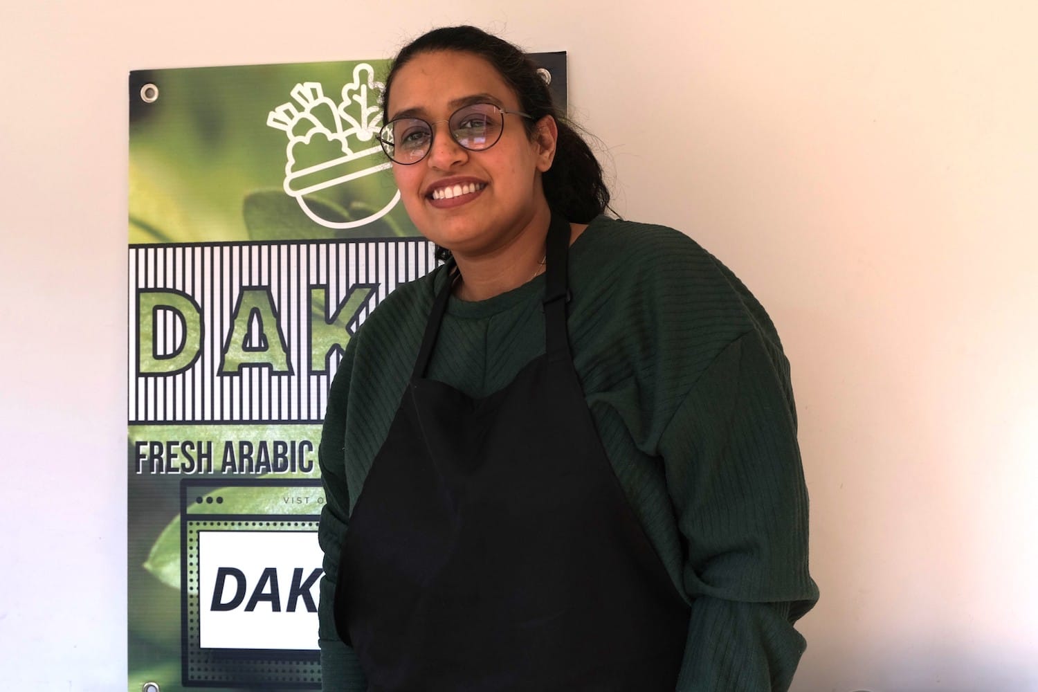 A woman stands in front f a green sign. She is smiling.