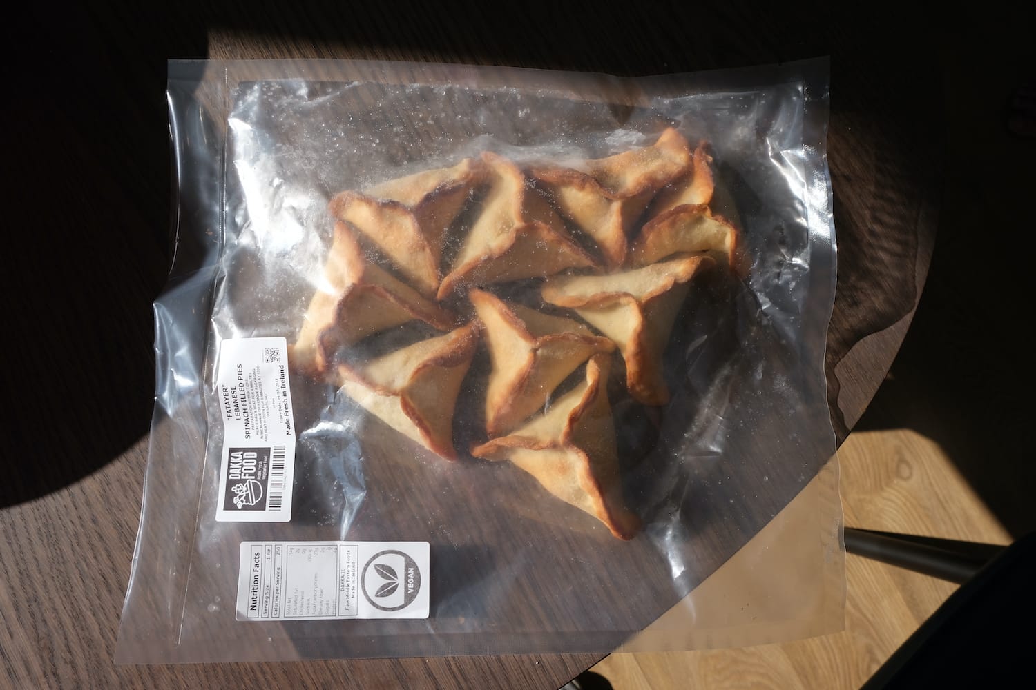 A transparent bag of triangular pies. A small white label on the bag says they are fatayer, Lebanese spinach pies.