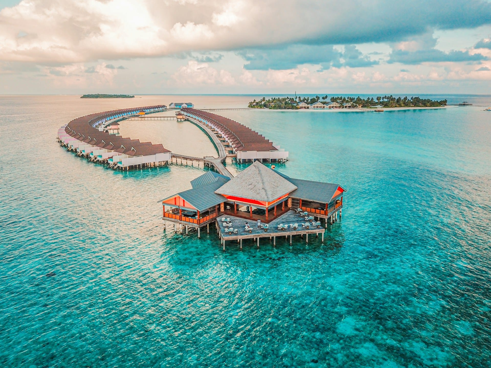 Curved wooden jetty leading to overwater villas across a Maldivian lagoon