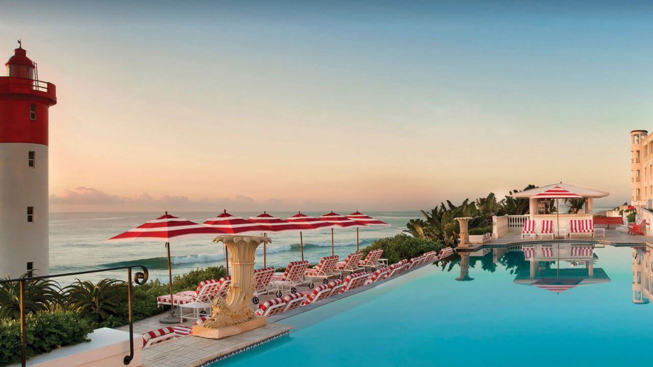 A coastal South African pool deck at golden hour, looking out to the Indian Ocean.