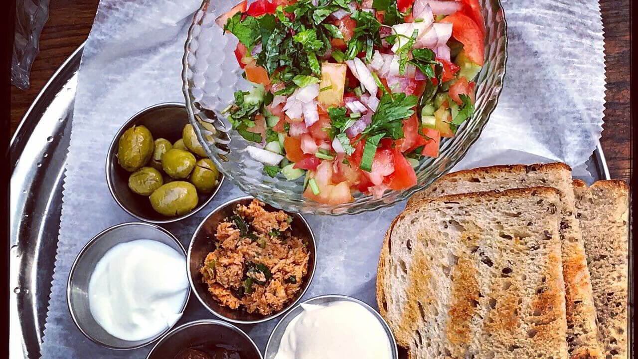 A kosher mezze platter with fresh salad, olives and warm bread.