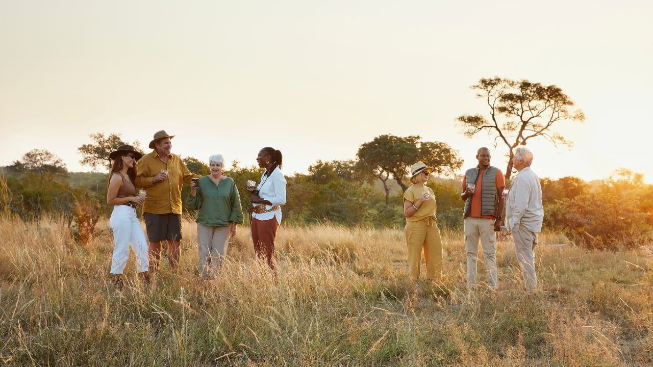 Three generations of a family on safari at golden hour, gathered in the long grass.