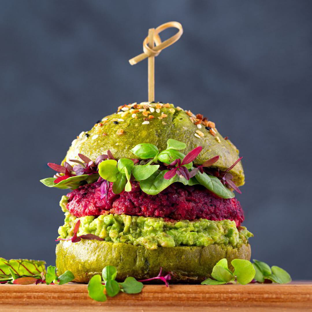 A plant-based beetroot burger with avocado on a green bun.