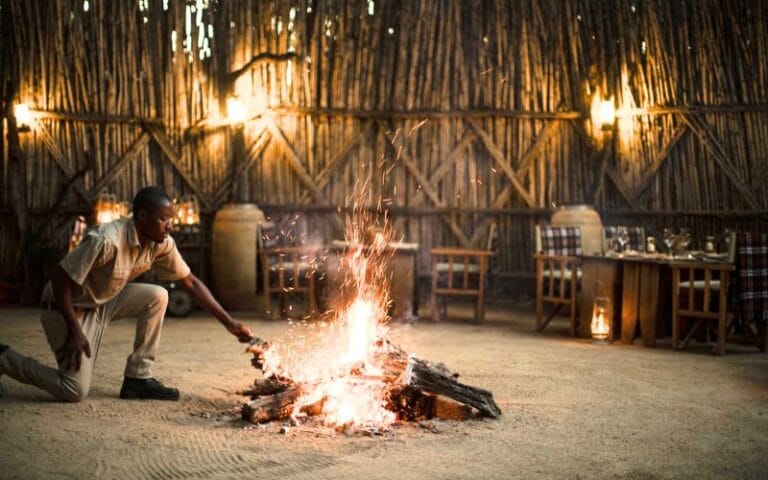 Private candlelit dinner table set on a wooden deck overlooking the African bush at night