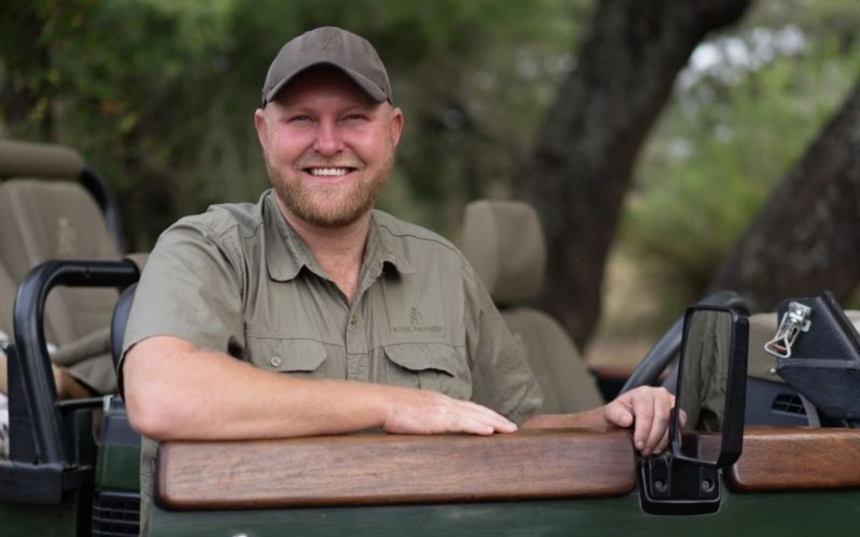 Field guide leaning on the bonnet of a safari vehicle in soft afternoon light, relaxed and smiling