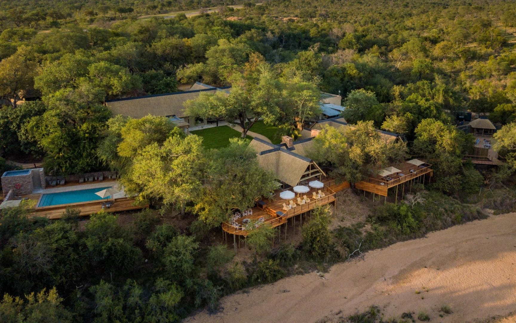 Aerial view of a thatched lodge on a Greater Kruger riverbank, deck and pool below the suites