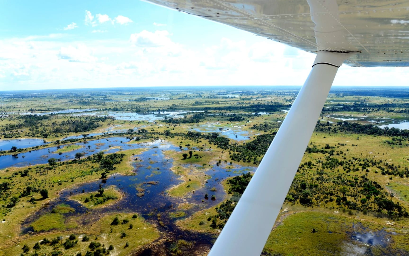 Light aircraft wing over the Okavango Delta channels, water and islands stretching to the horizon