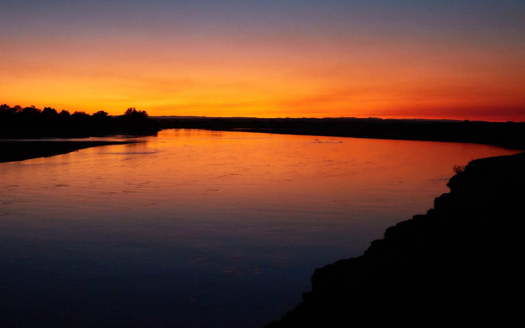 Zambian river at sunset, dark indigo sky above deep orange light reflecting off the water