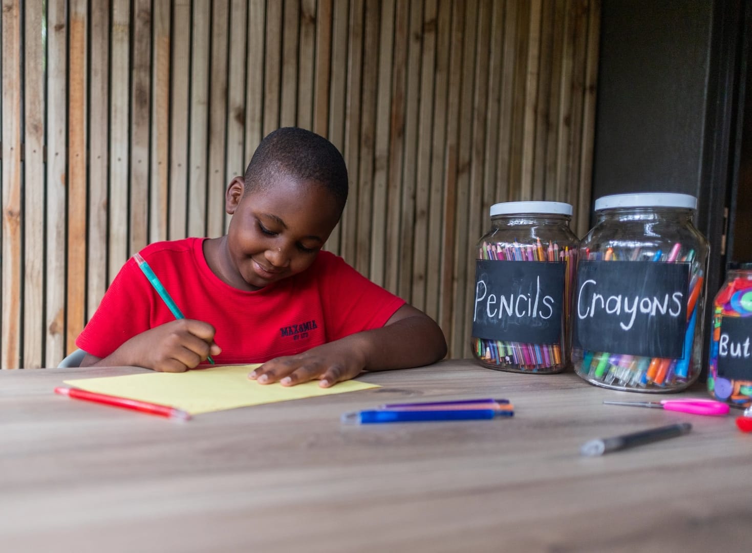 A young guest drawing at the lodge kids' table between game drives, pencils and crayons laid out