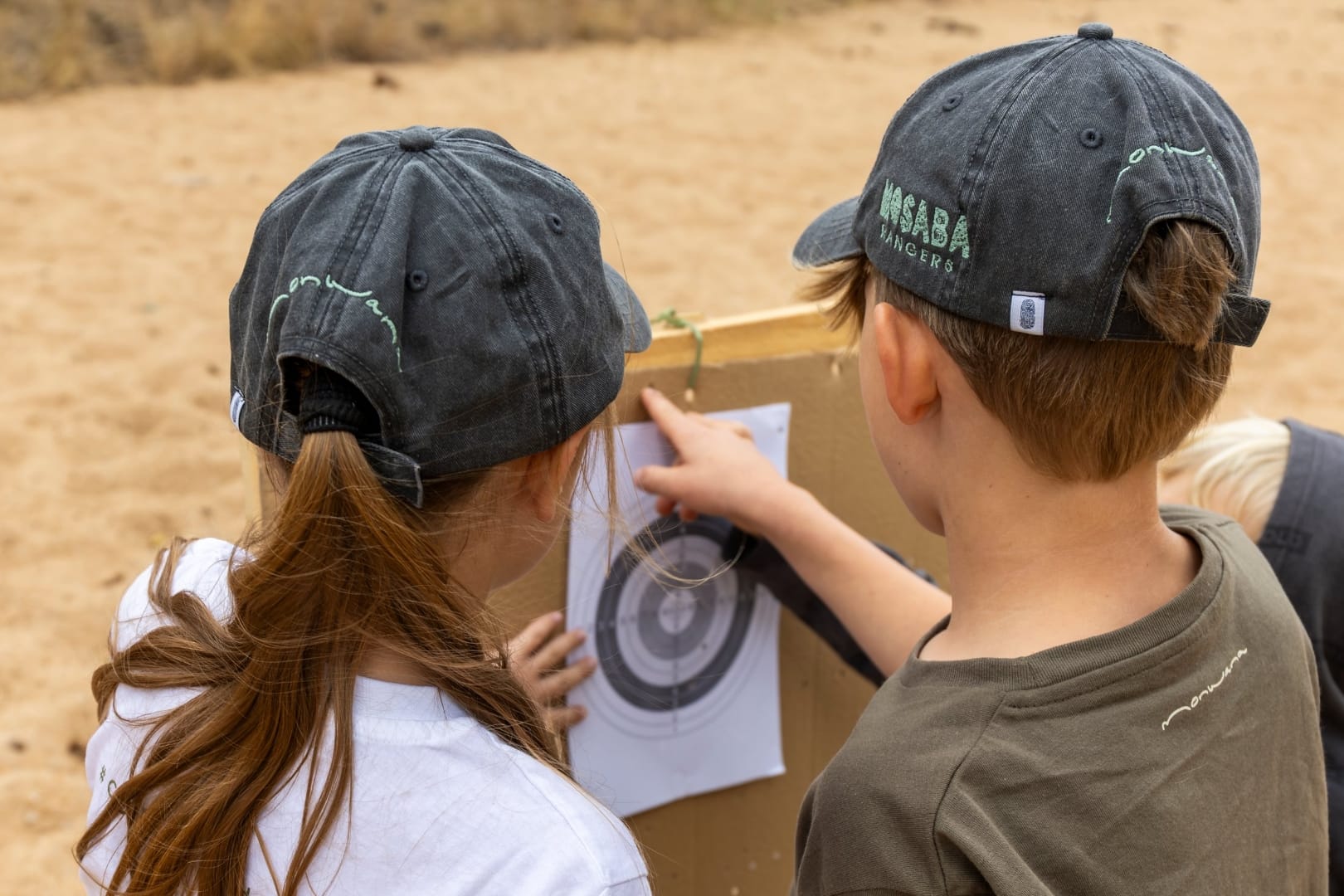 Two young guests in safari caps with a paper target between activities, a quiet moment at the lodge