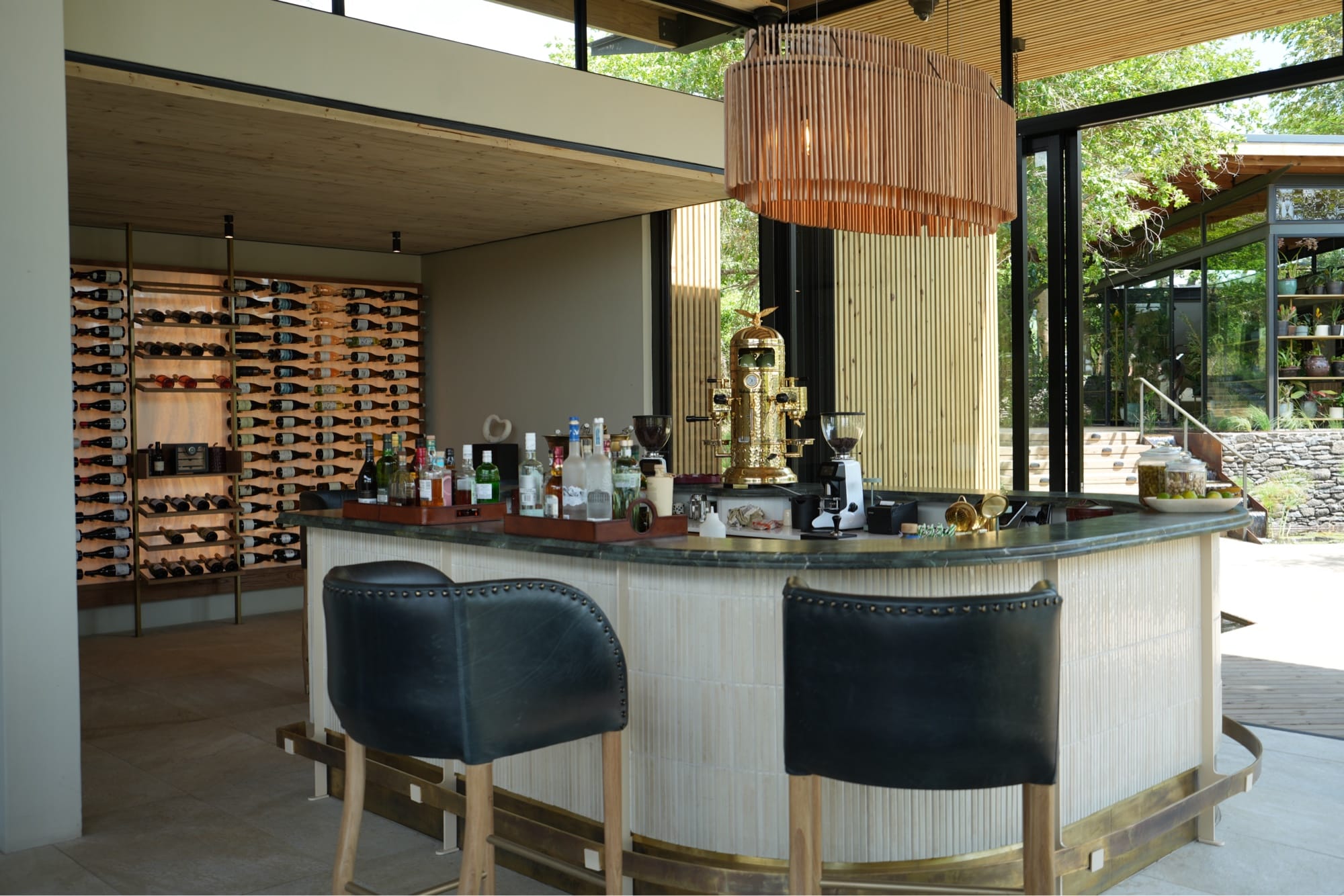 Curved bar with gold espresso machine, copper pendant lamp, and backlit wine wall at Lion Sands Ivory Lodge