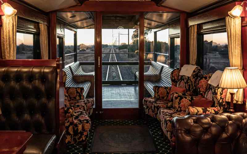 Rovos Rail observation car with vintage leather armchairs and panoramic windows at sunset