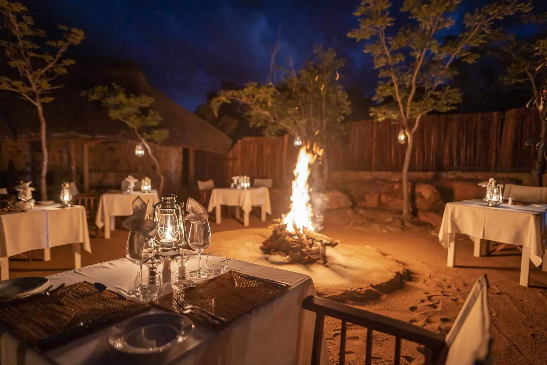 Guests dining at the Tshwene Boma, with lanterns and firelight illuminating a long table set in the open bush