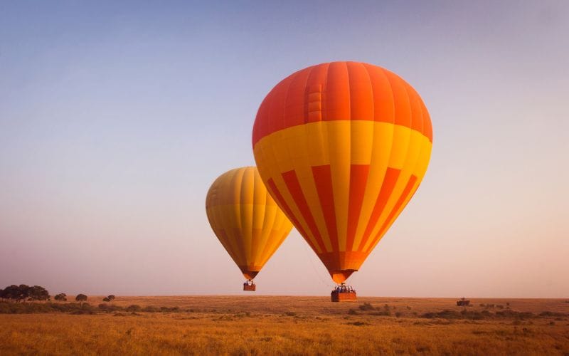 Hot air balloon drifting over the South African bushveld at sunrise, the landscape golden below
