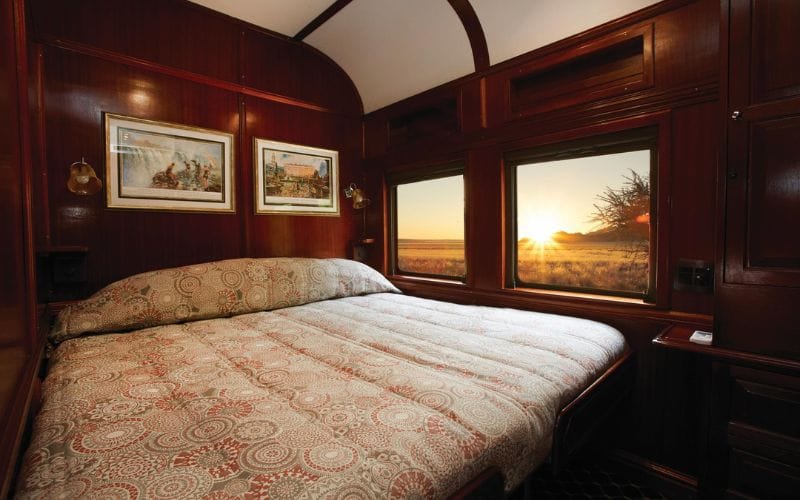 Rovos Rail suite interior with polished mahogany panelling, brass fittings and double bed with white linen