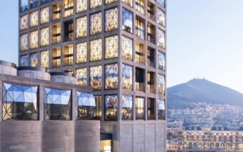 A suite at The Silo Hotel with a freestanding bathtub positioned in front of a curved pillowed glass window, Table Mountain visible beyond