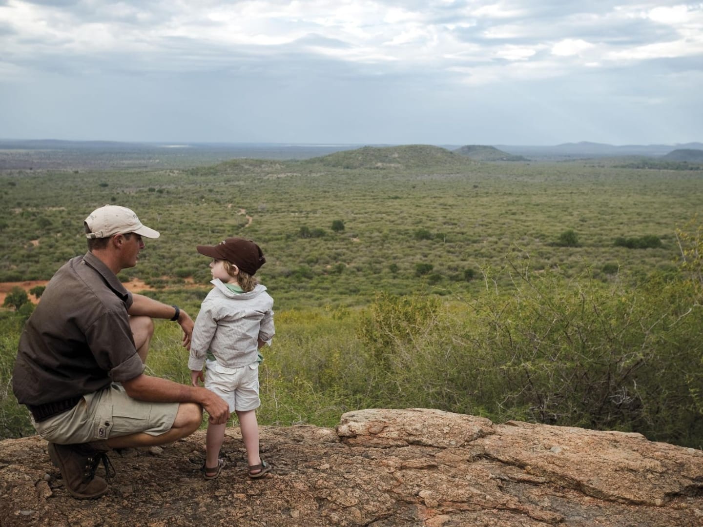 A father and his young son crouched on a rocky koppie in Madikwe, looking out across the malaria-free bushveld