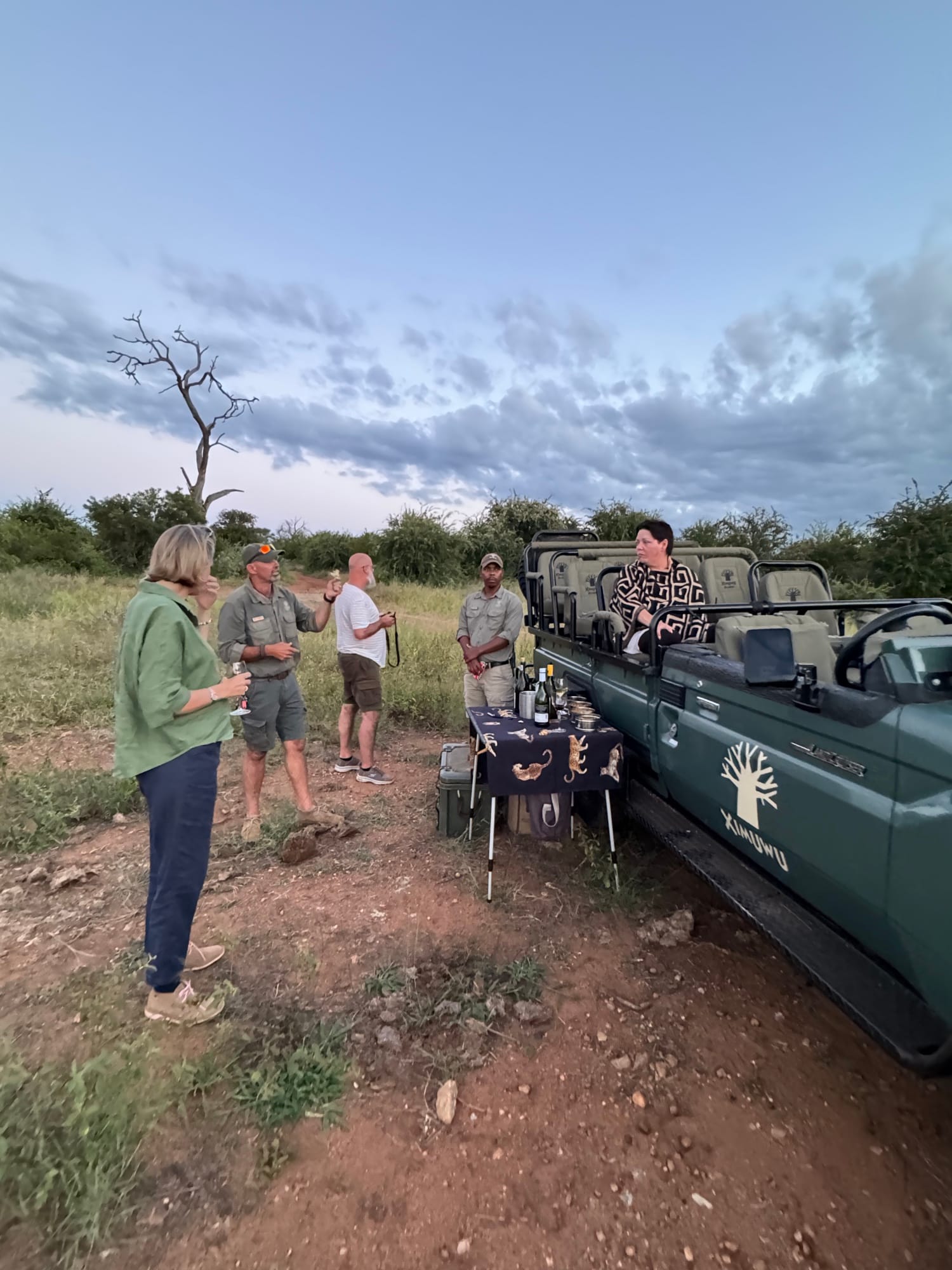 Guests and guides at sundowner drinks beside a safari vehicle in the bush