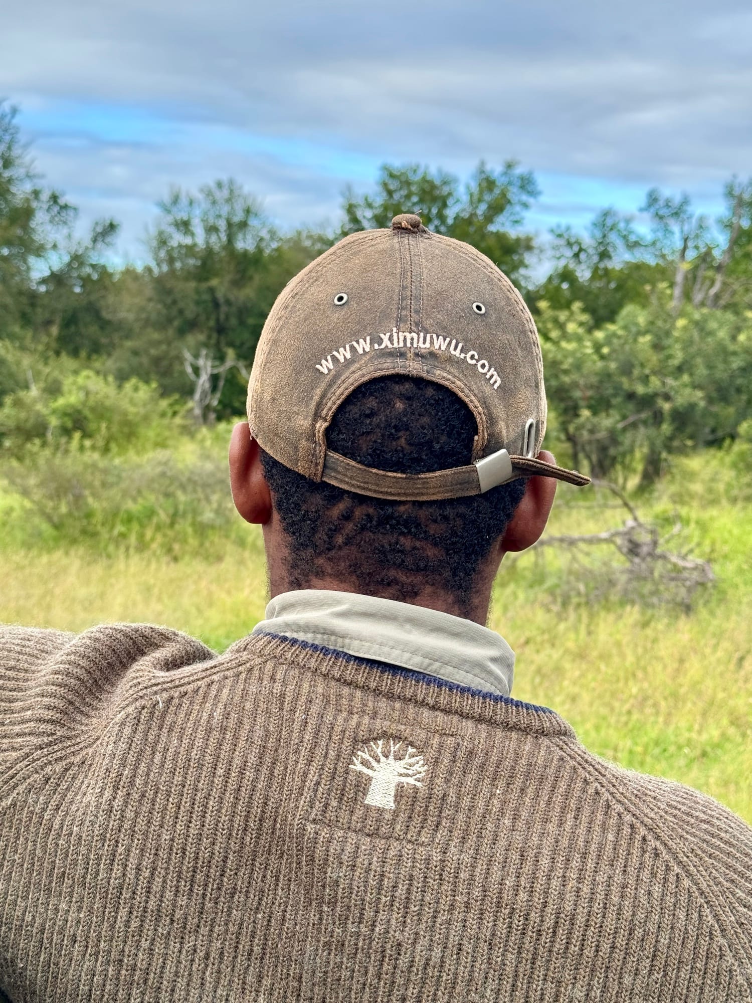 Safari tracker from behind wearing a Ximuwu cap, looking out over the bush