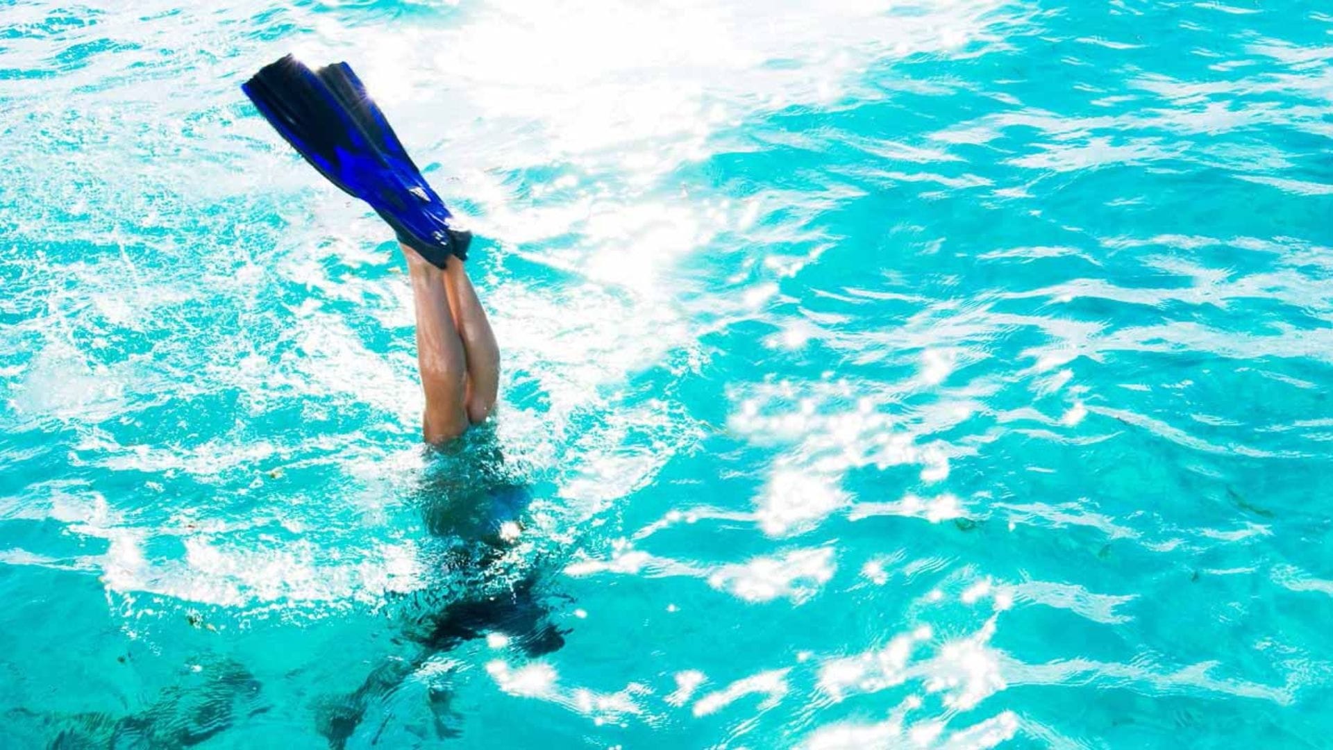 Snorkeller diving feet-first into clear turquoise water with sunlight on the surface, Mozambique