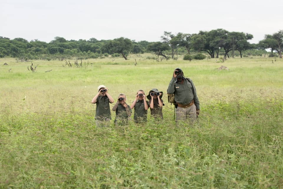 Safari guide and three young guests on a walking safari in the bush, all on binoculars