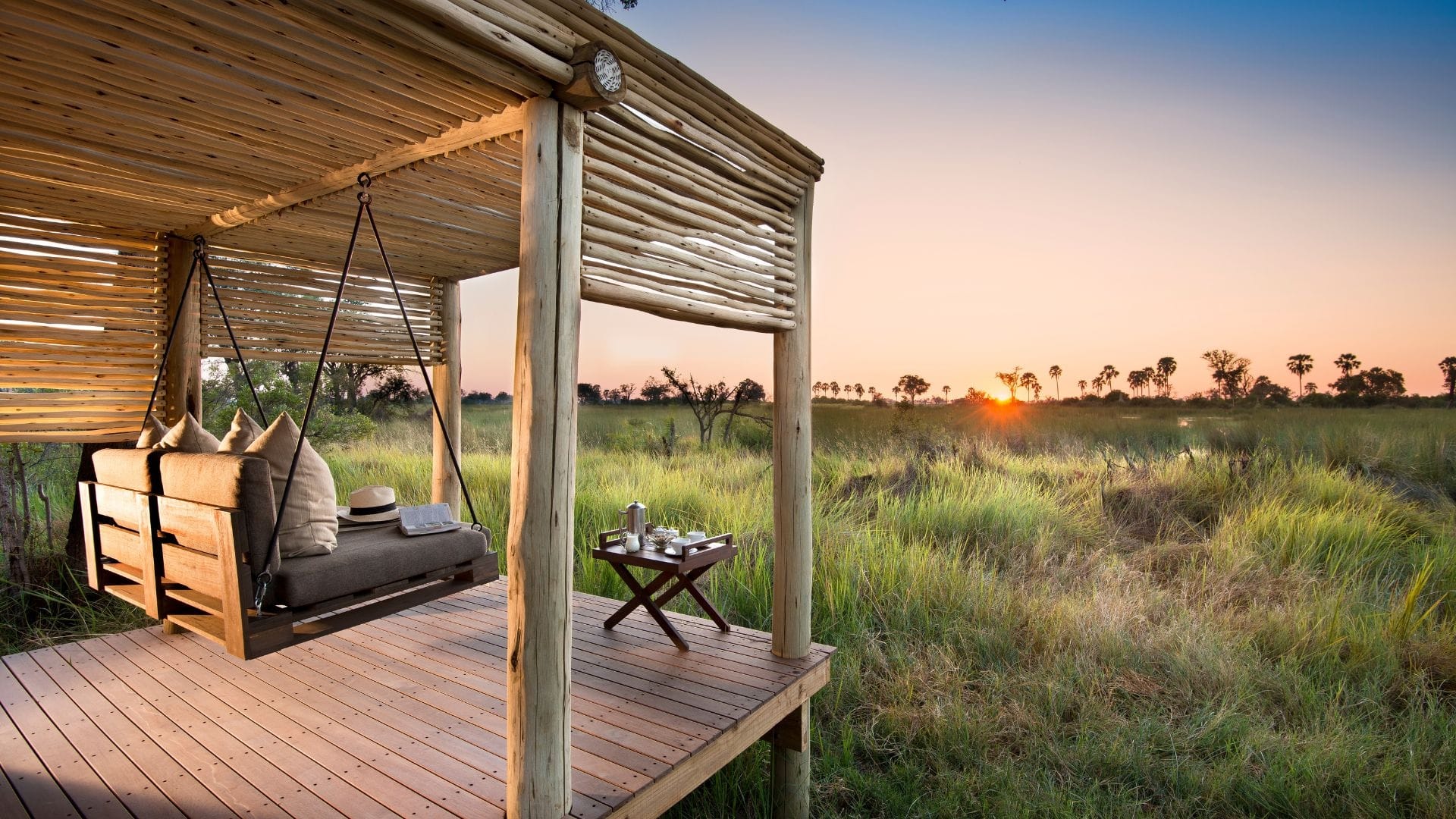 A private deck with a daybed swing overlooking the Okavango Delta floodplain at sunset
