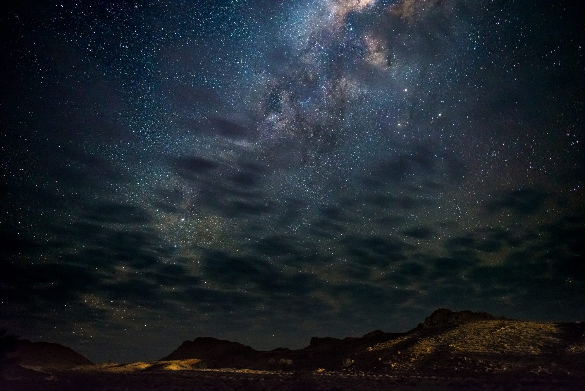 The Milky Way arching over the NamibRand at night, the dune line silhouetted along the horizon