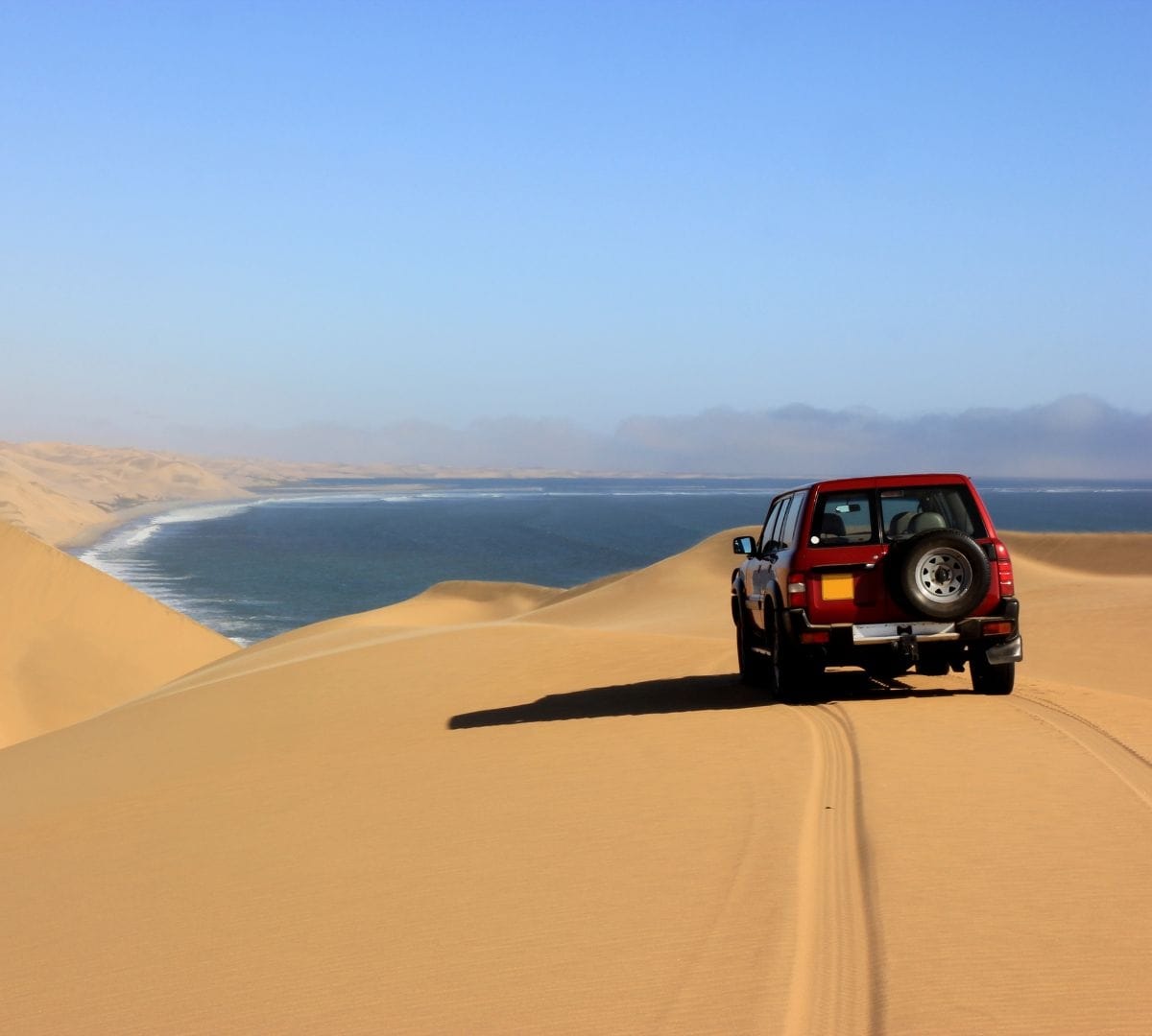 A 4x4 cresting a sand dune on the Skeleton Coast, the Atlantic Ocean meeting the Namib desert on the horizon