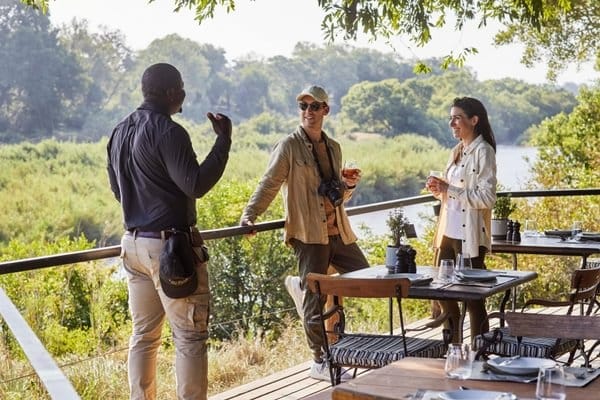 Guide pouring sundowners for a couple on a private lodge deck at dusk