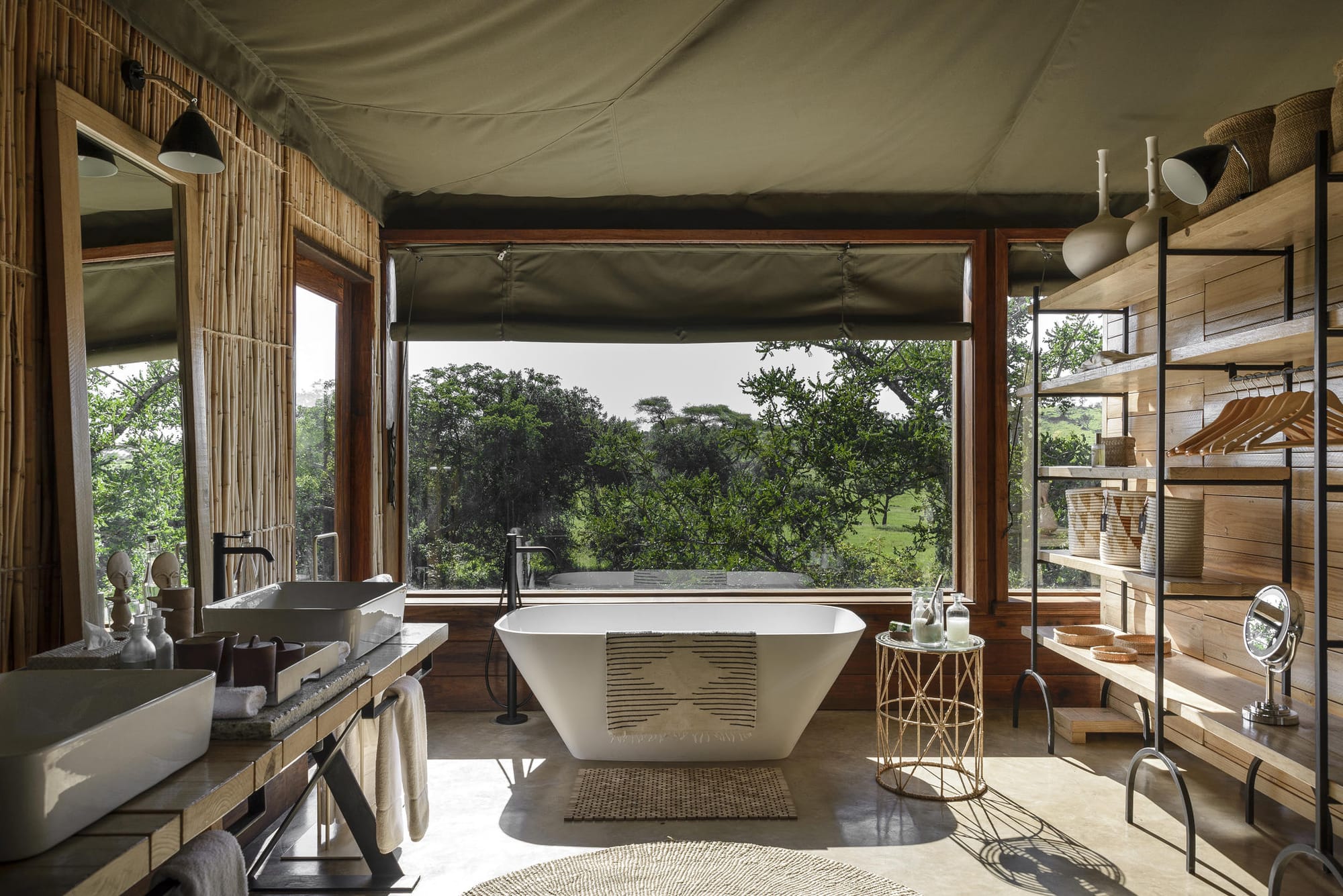A freestanding bath in a tented suite at Singita Faru Faru, framed by full-width windows looking onto the Grumeti bush