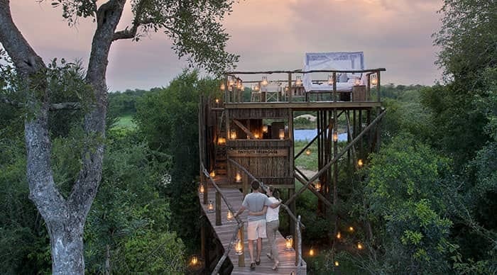 A couple walking by lantern light along the boardwalk to the Tinyeleti Treehouse at Lion Sands, with the open-air bed visible above