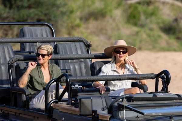 Couple wrapped in blankets on the back bench of an open game vehicle at first light