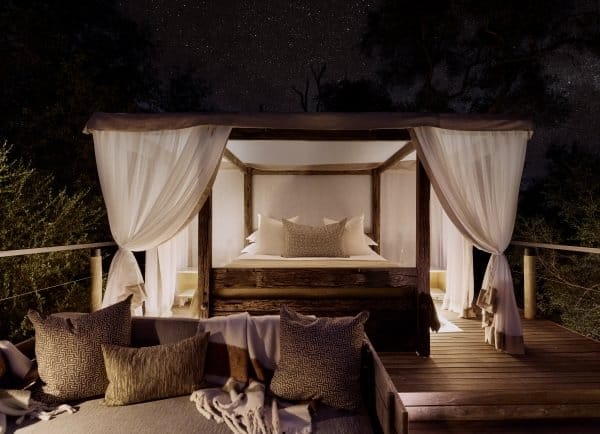 Canopy sleep-out bed on a raised platform, layered with linen and pillows