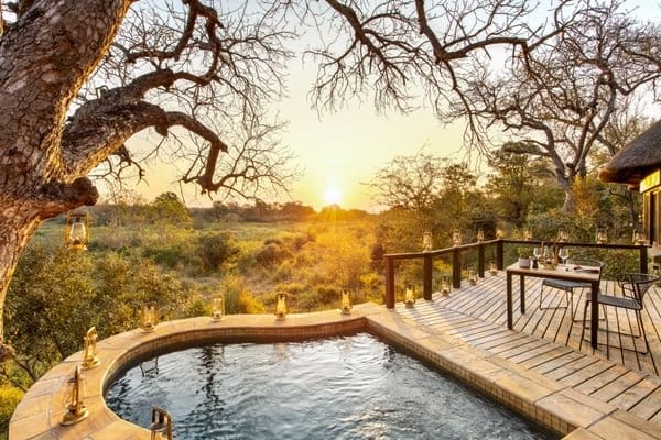 Sunset plunge pool on a lodge deck with an open fire pit and lantern glow