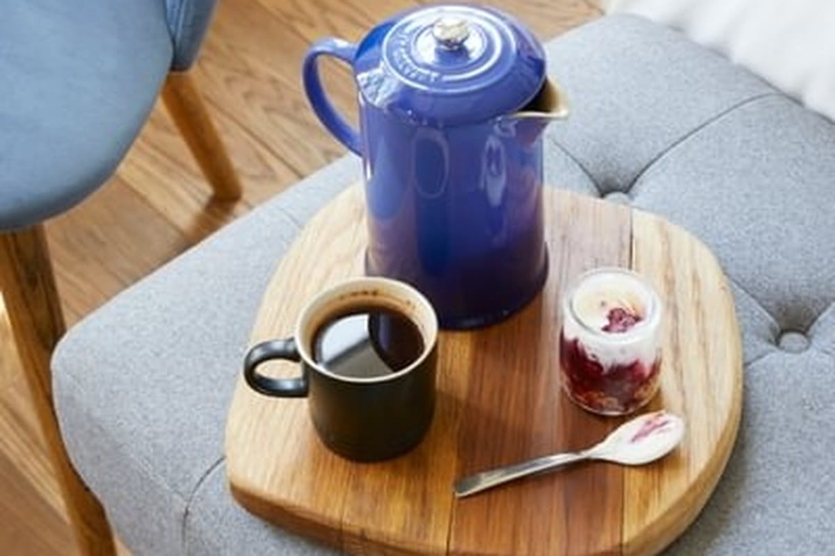 Coffee tray on a circular wooden board, blue enamel coffee pot, dark mug of coffee, small jar of compote, a quiet pre-dawn lodge detail