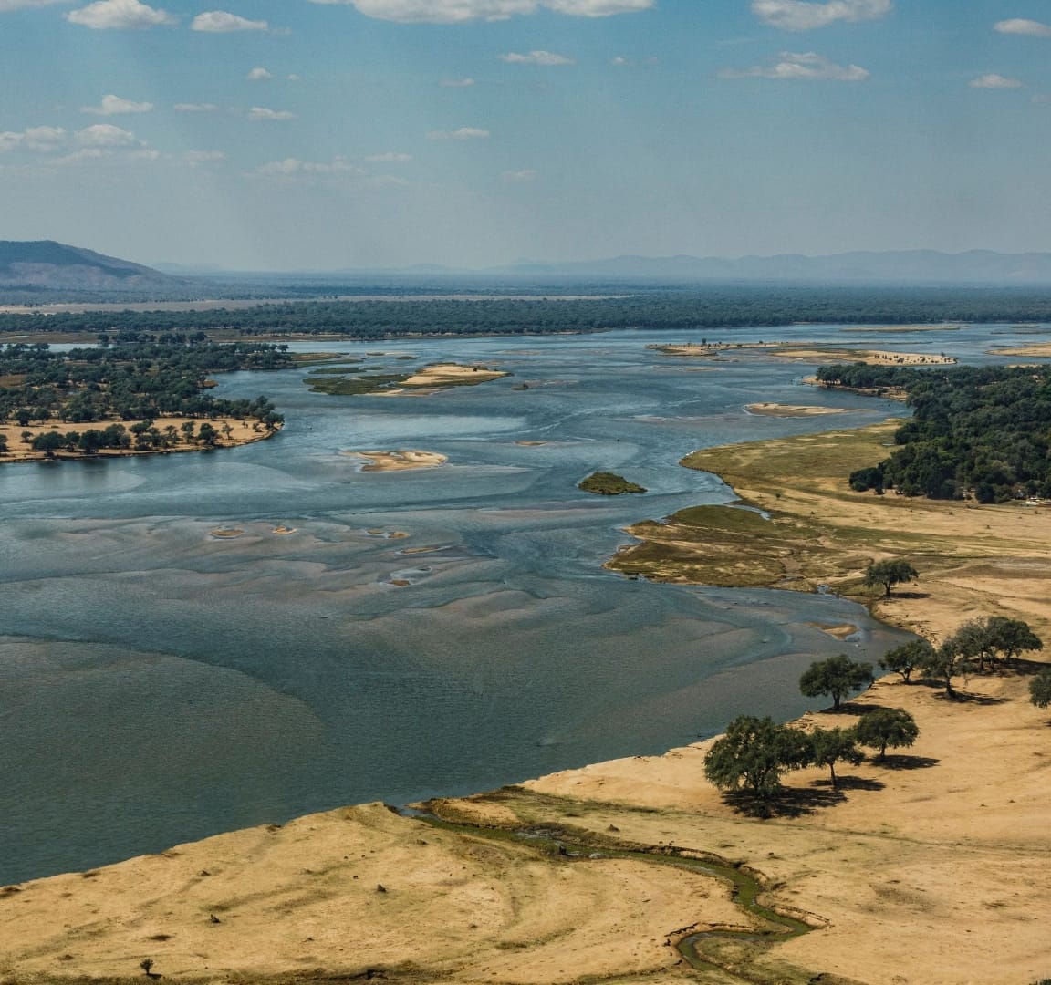 Aerial view of the Lower Zambezi River with sandbars and riverine forest, the Zambian bank in the foreground and the Mana Pools escarpment of Zimbabwe rising in the distance