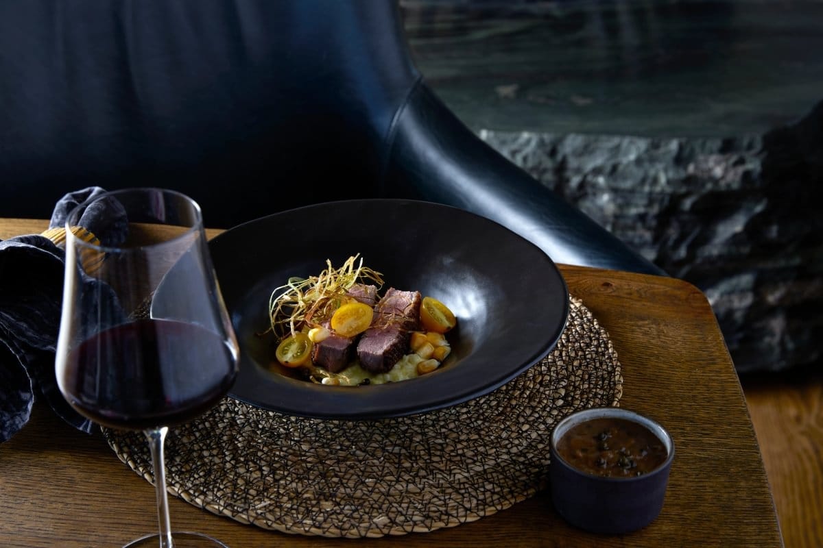 Duck breast on sweetcorn risotto with a glass of red wine on a dark wooden table